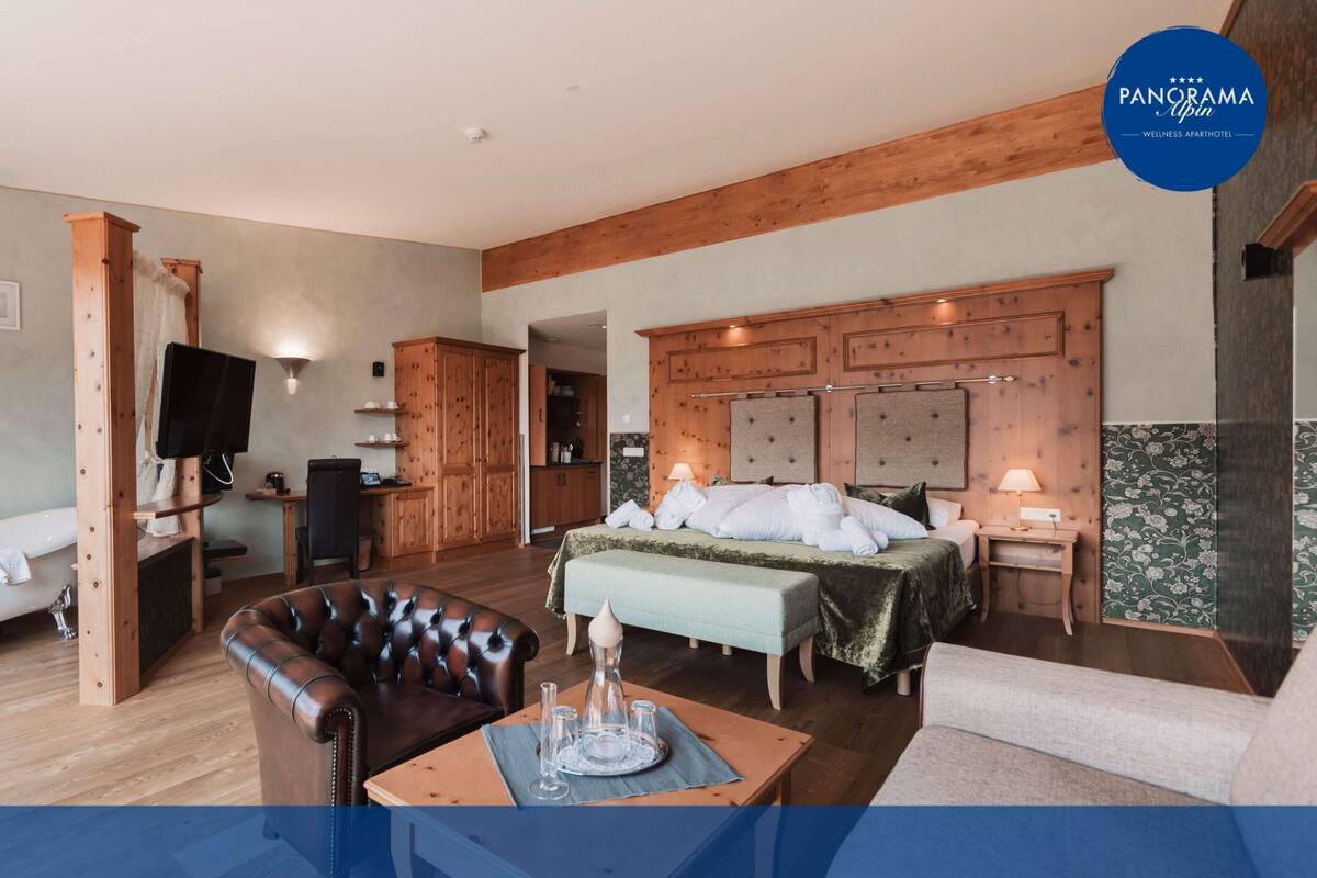 Une chambre élégante, dotée d’un grand lit, d’un coin salon avec un fauteuil en cuir, d’un bureau en bois et d’une baignoire.
