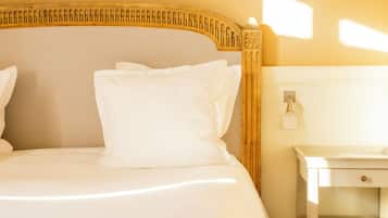Una cama bien hecha con sábanas y almohadas blancas, un cabecero de madera con un diseño decorativo y una mesita de noche sencilla con una lámpara.