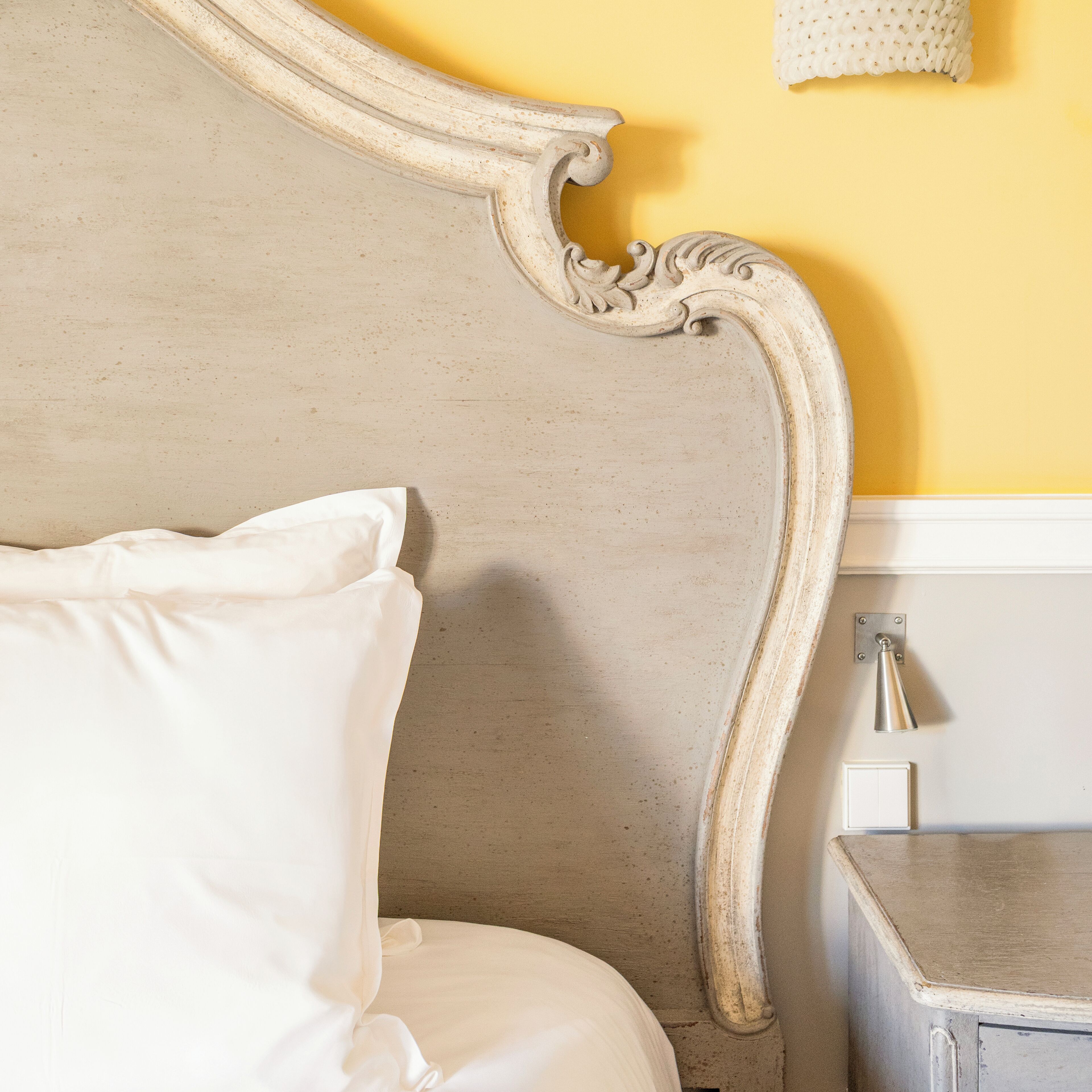 A bed with a headboard, a bedside table, and a wall-mounted lamp.