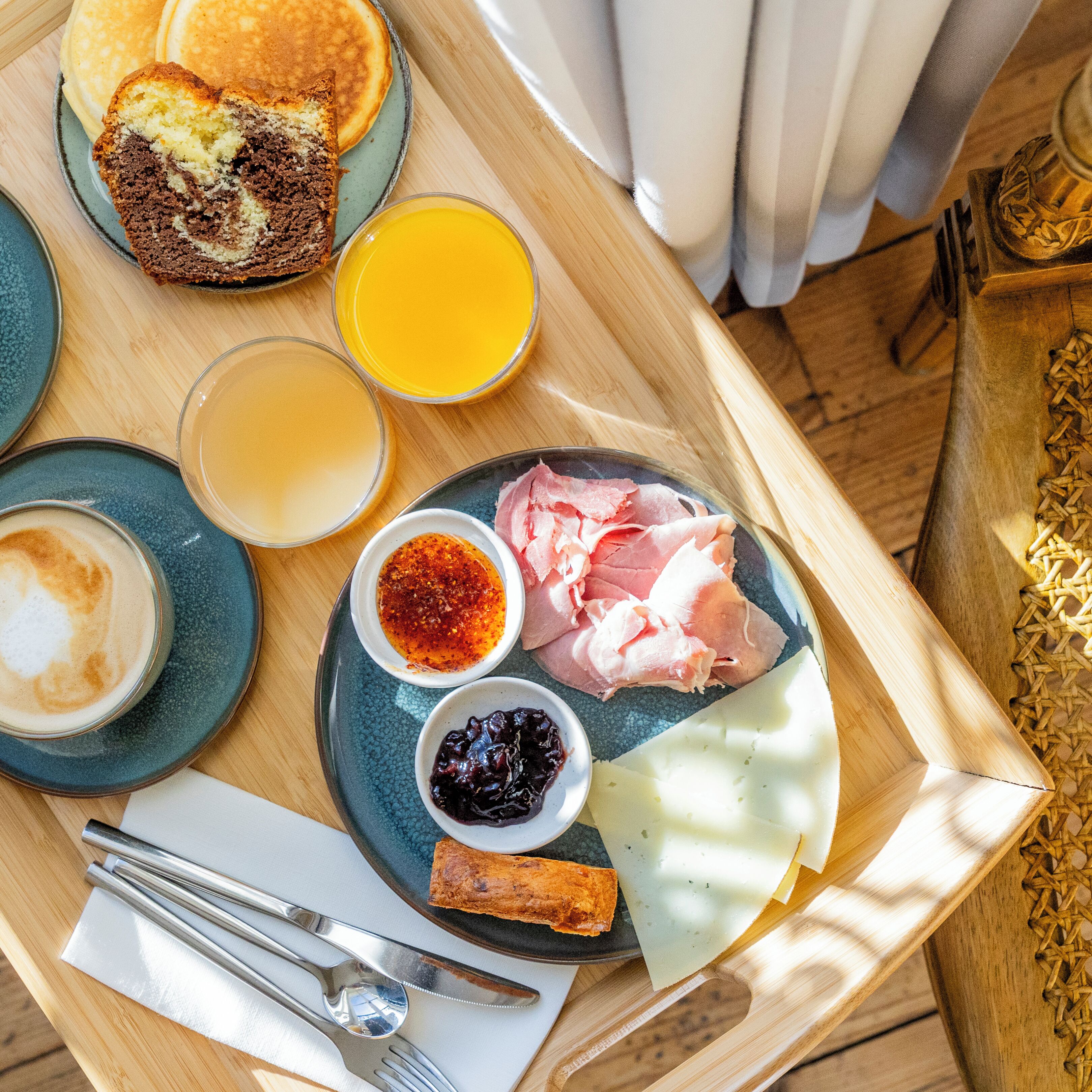 En bakke med morgenmad bestående af pandekager, appelsinjuice, kaffe, skinke, ost og tilbehør.