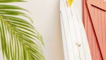 A surfboard leaning against a wall with a palm leaf in the foreground.