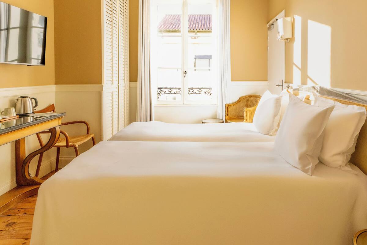 Ein Hotelzimmer mit Bett, Schreibtisch, Stuhl, Fernseher und einem Fenster mit Vorhängen.