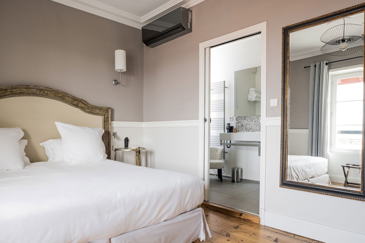 A bedroom with a large bed, a mirror, a bedside table, and a bathroom visible through an open door.