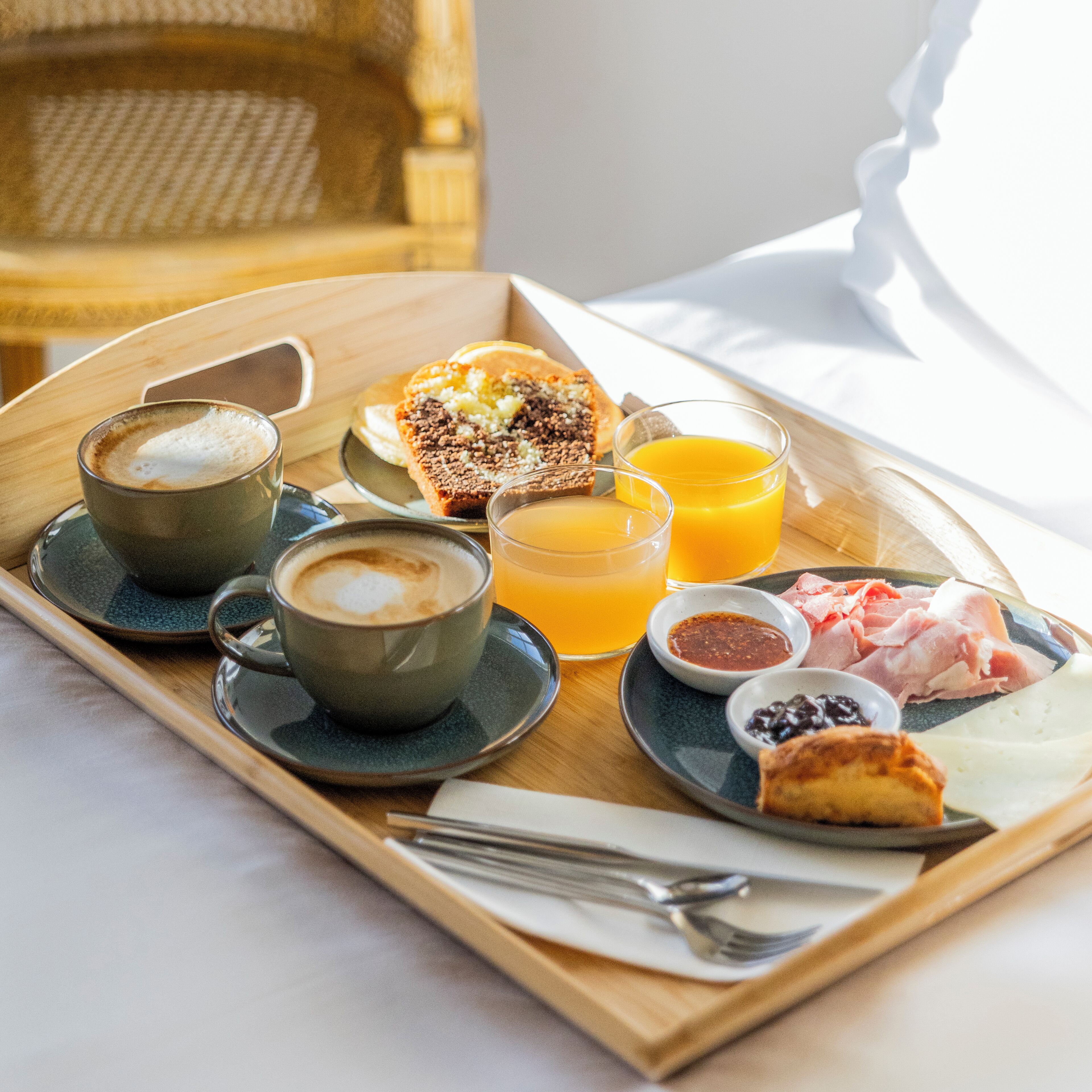 A breakfast tray with coffee, orange juice, pastries, and meats on a wooden tray.