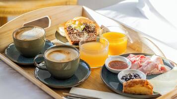 Una bandeja de desayuno con café, zumo de naranja, bollería y embutidos sobre una bandeja de madera.