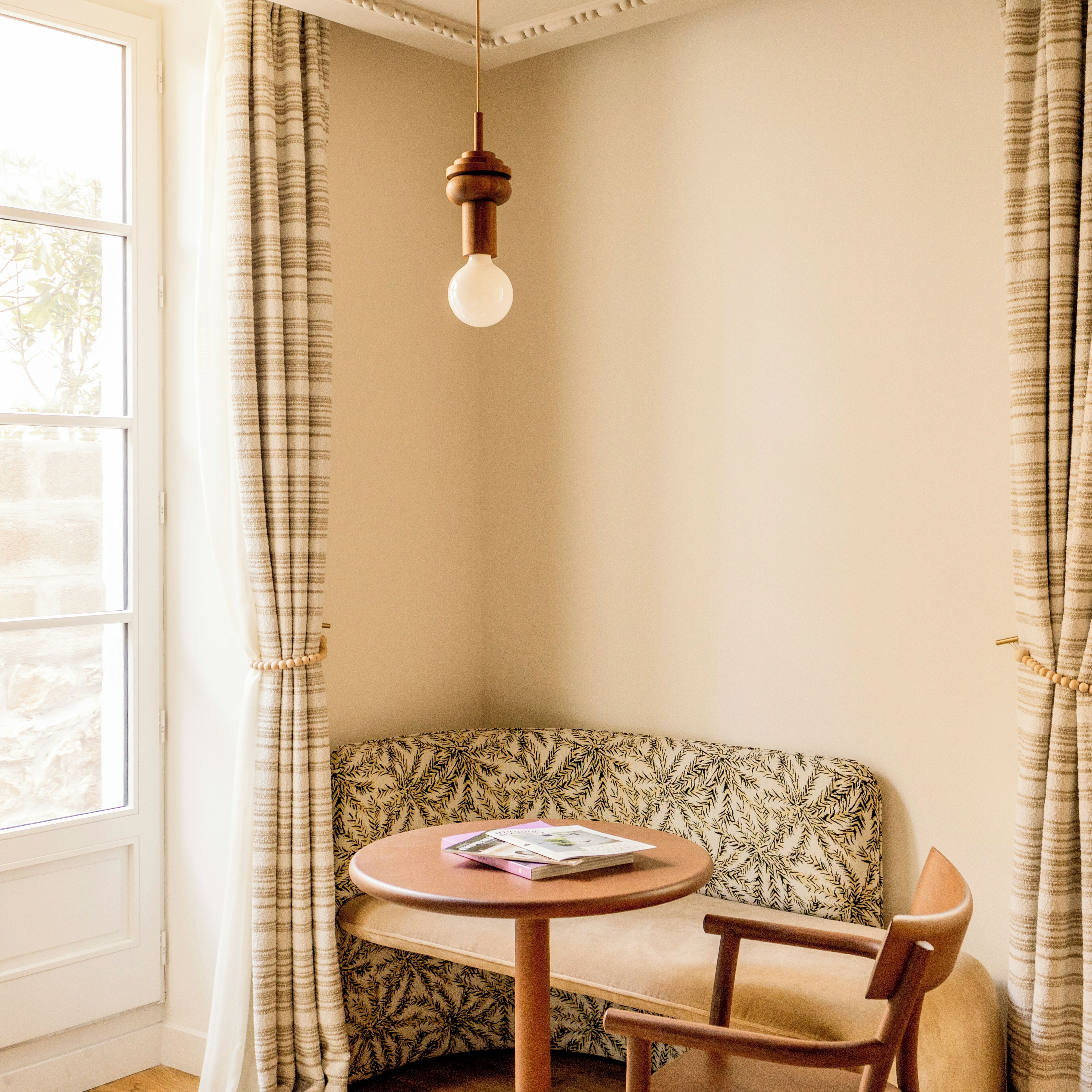 A corner seating area with a patterned sofa, a round wooden table, and a hanging light fixture.