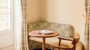 A corner seating area with a patterned sofa, a round wooden table, and a hanging light fixture.