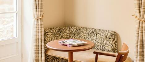 A corner seating area with a patterned sofa, a round wooden table, and a hanging light fixture.