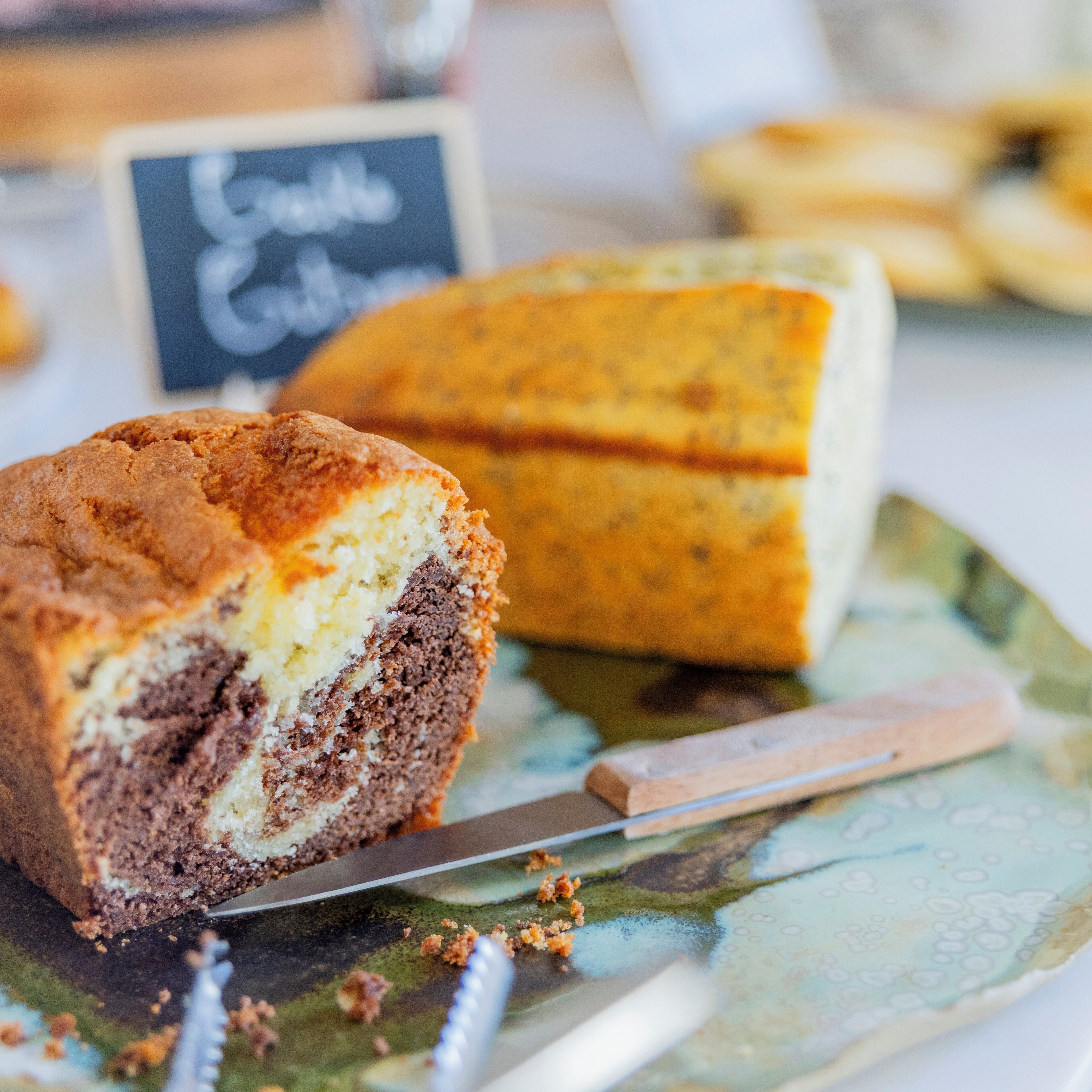 A slice of cake on a plate with a knife, and a whole cake in the background.