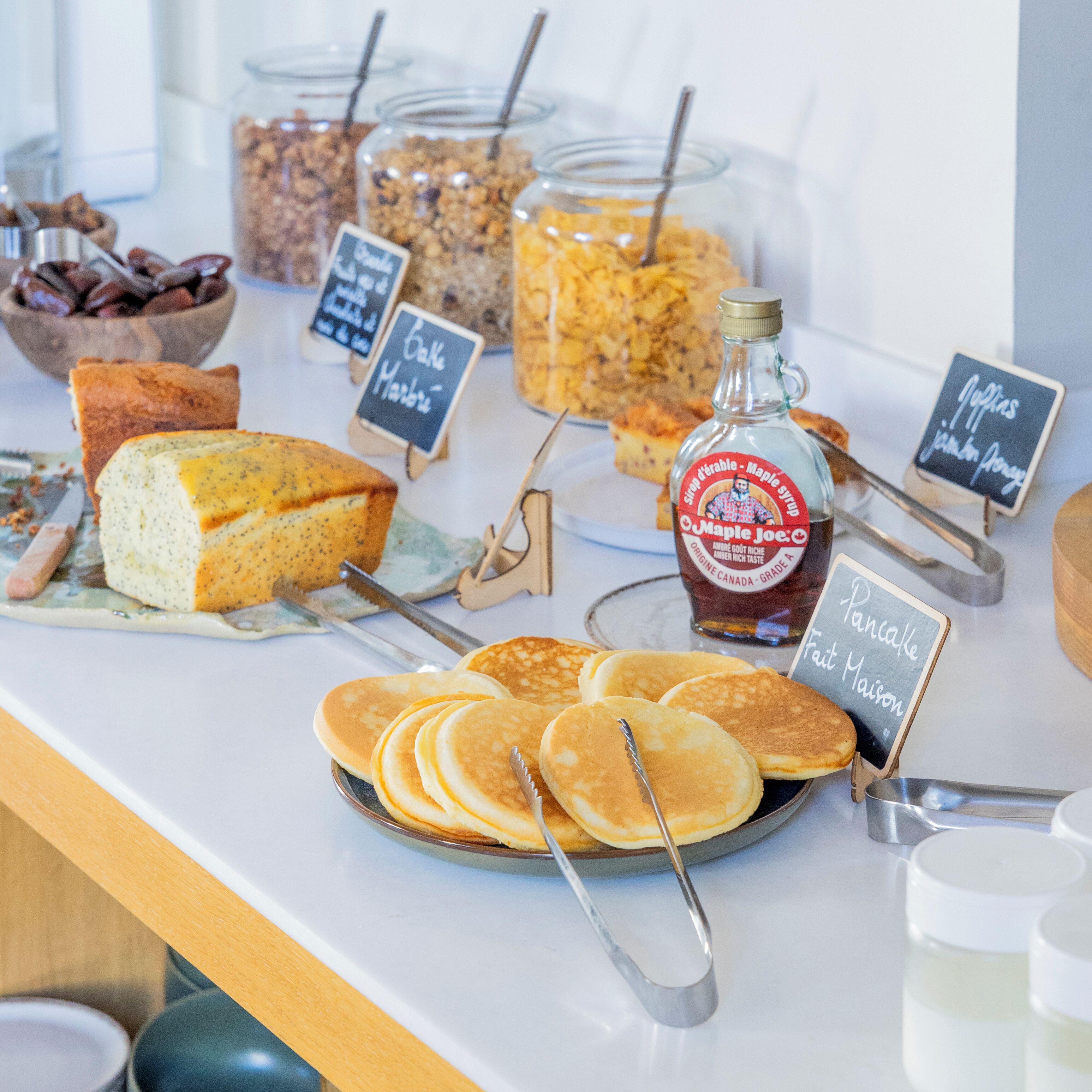 A breakfast buffet with pancakes, granola, and maple syrup.
