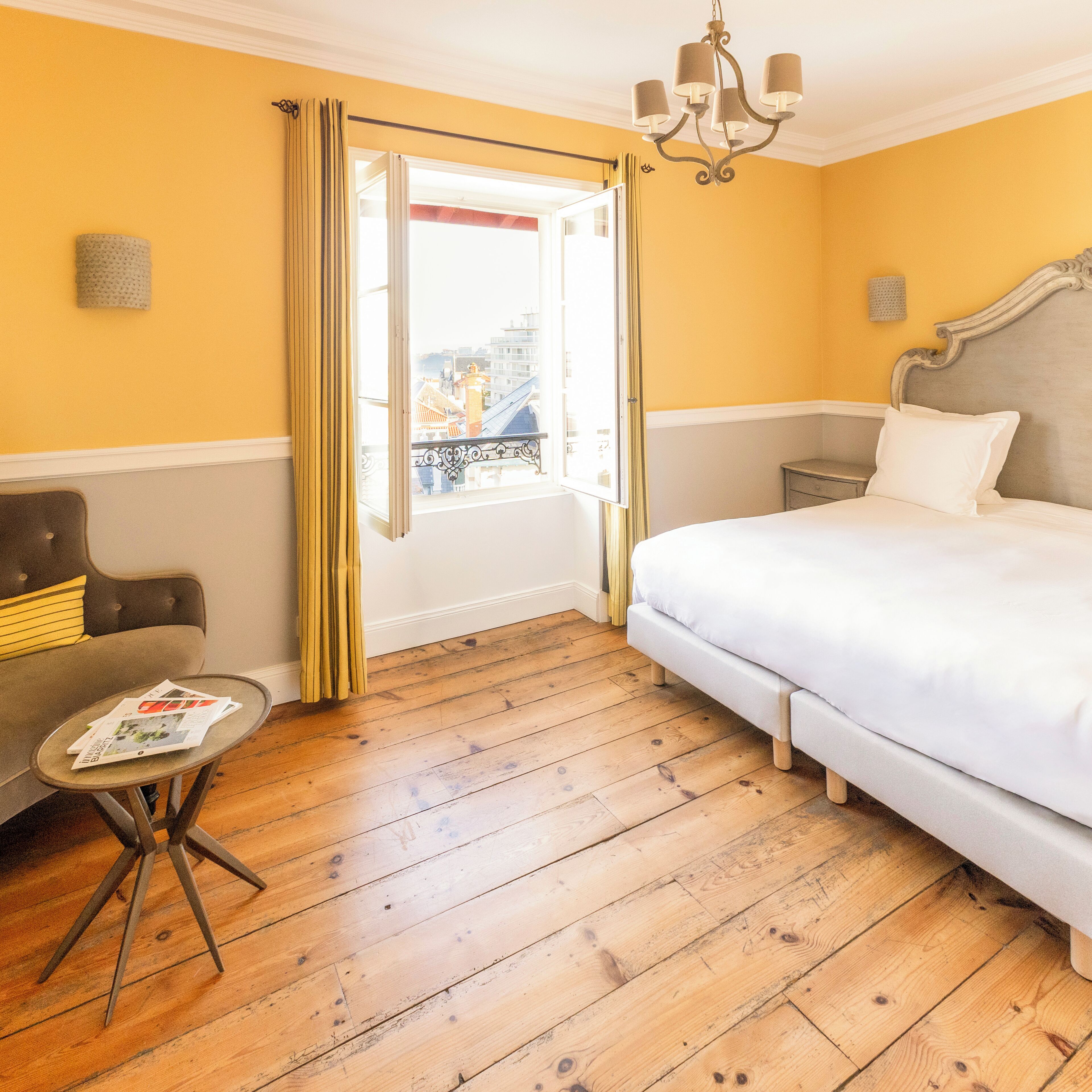 Una habitación de hotel con una cama, una mesita, un sofá y una ventana con cortinas.