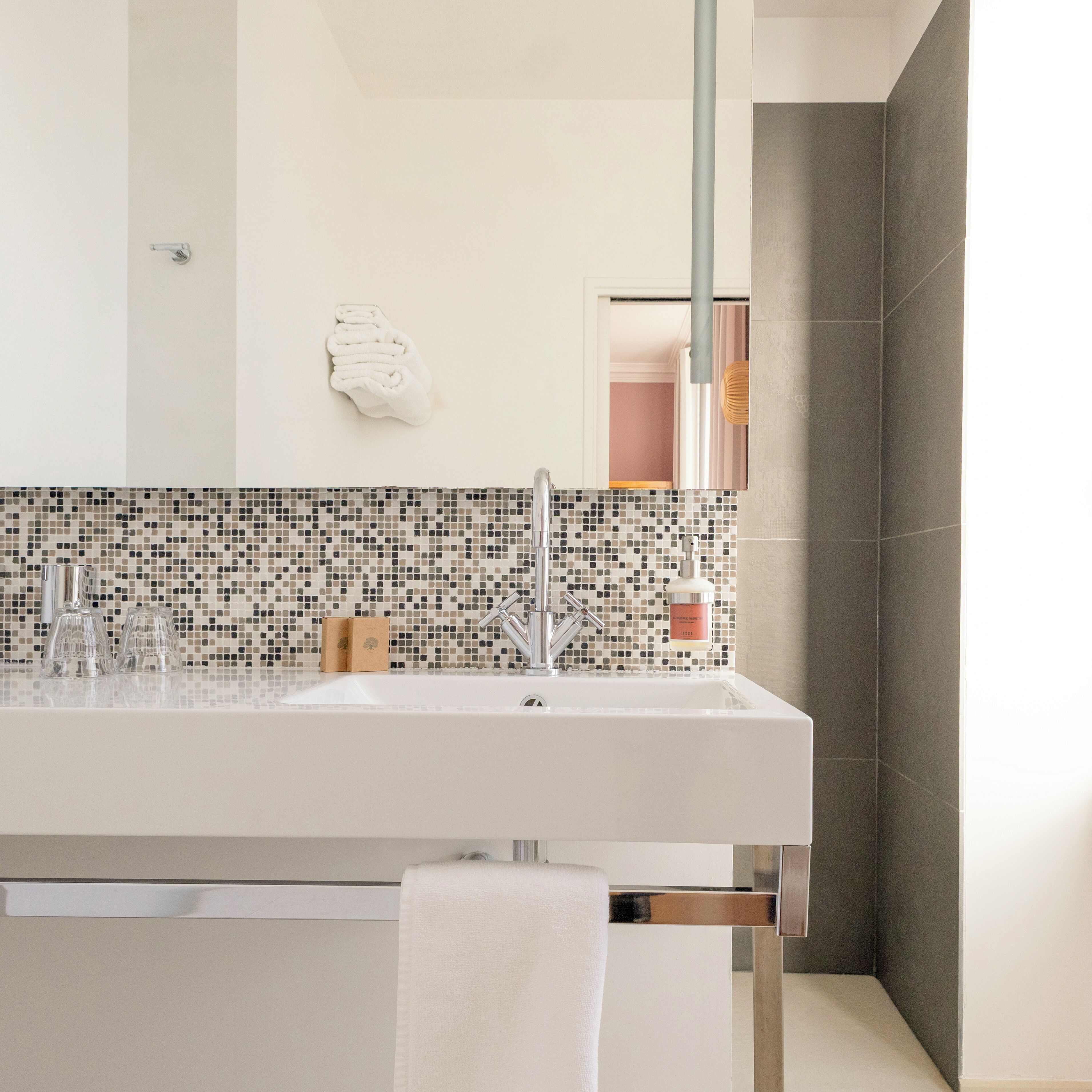 Une salle de bain moderne avec un lavabo blanc, un robinet chromé et un pare-feu en mosaïque.