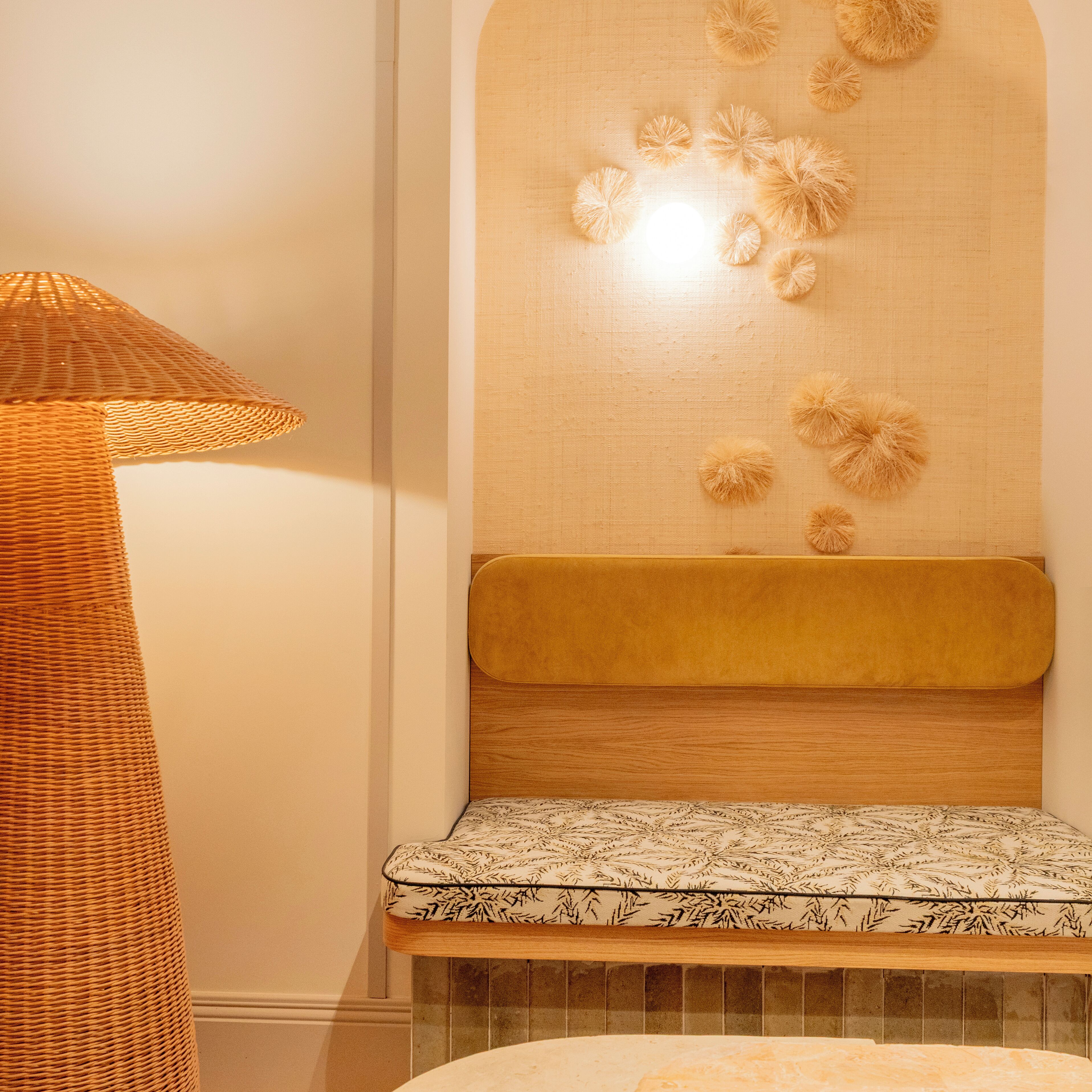 Quarto com luminária de chão trançada, cabeceira com almofada estofada e um banco estampado.