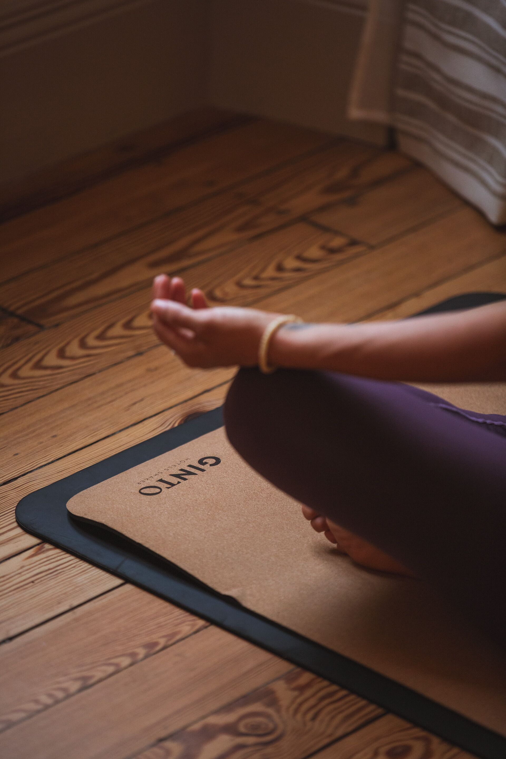 A person sitting on a yoga mat on a wooden floor.