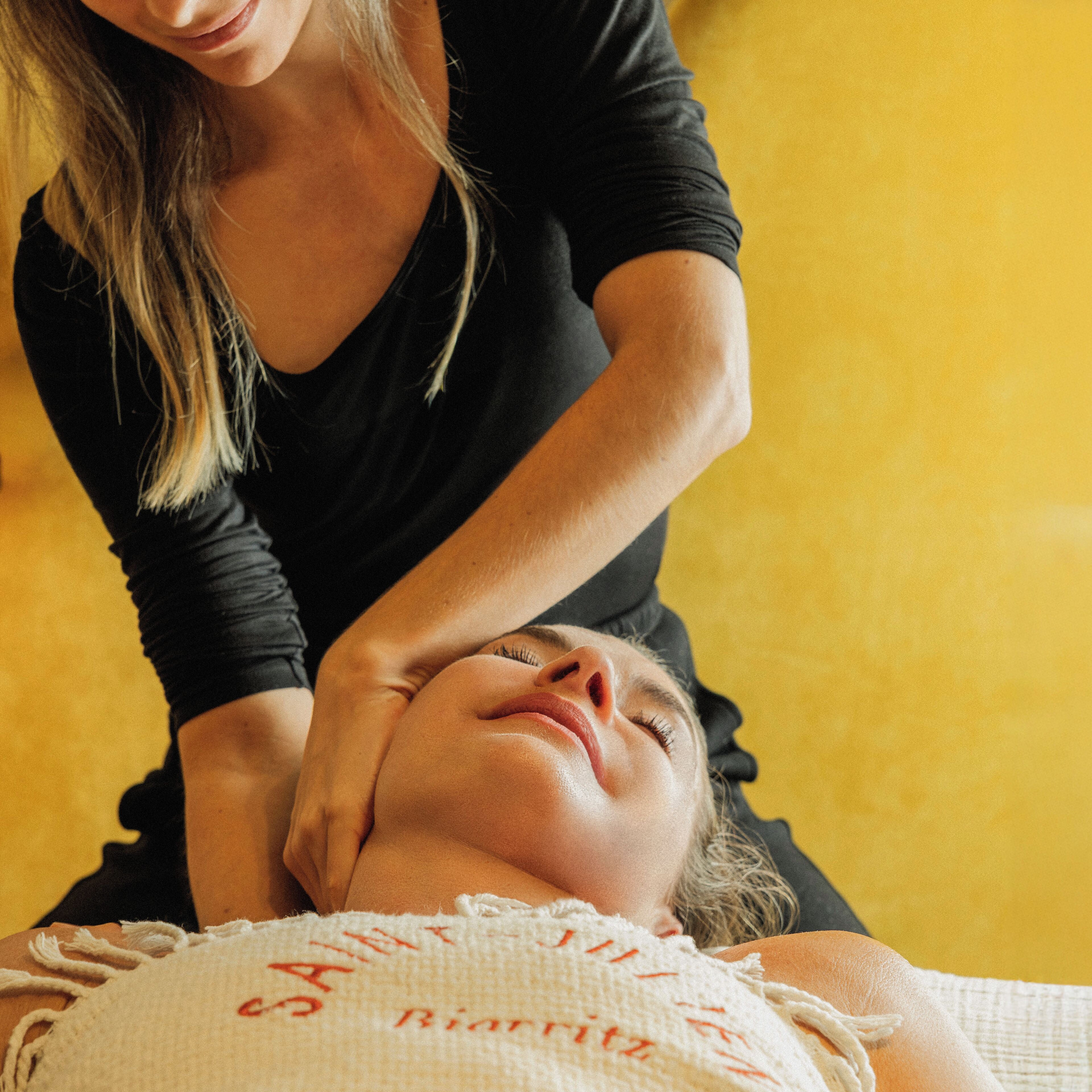 A person lying on a bed with a white pillow, receiving a massage from another person.