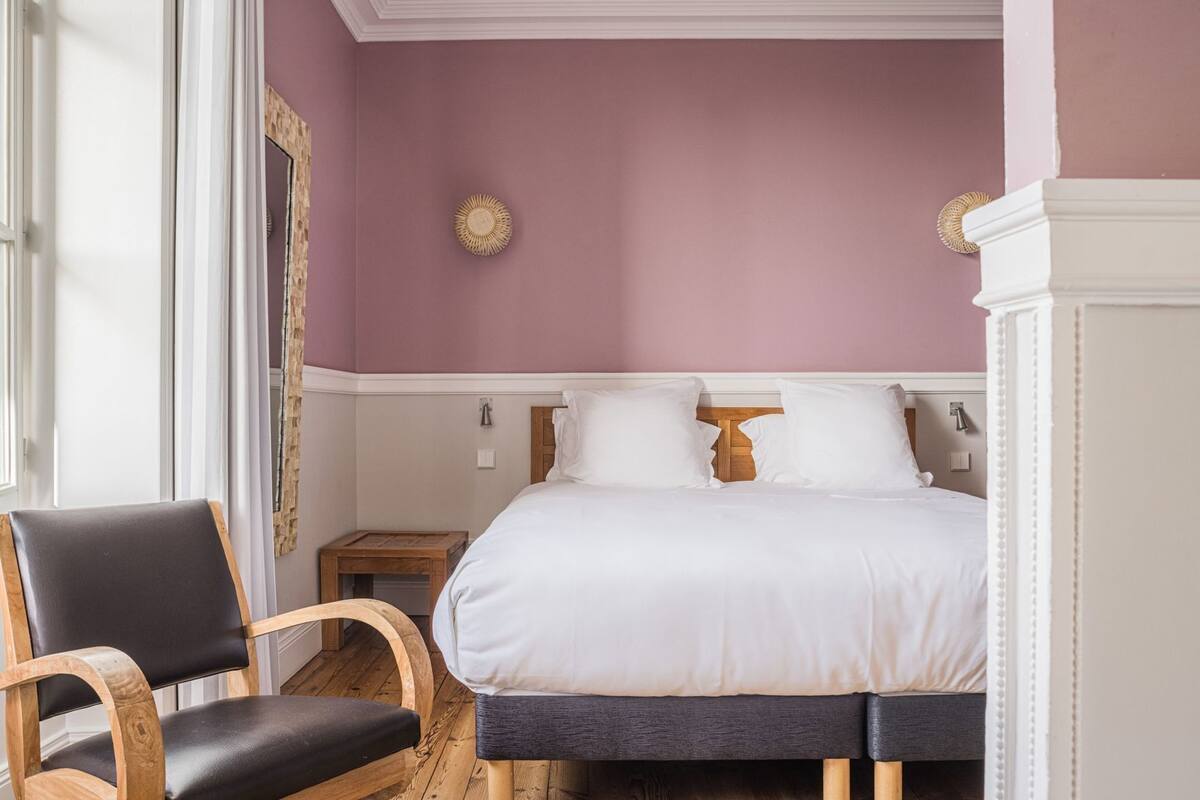 Ein Schlafzimmer mit einem Bett, Nachttischen, einem Sessel und einem Spiegel.