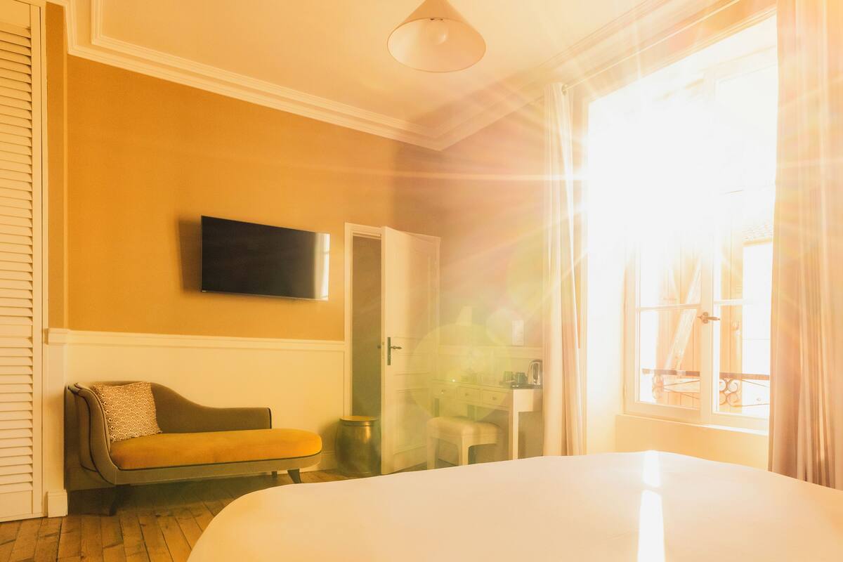 Ein Schlafzimmer mit einem großen Bett, einem Sofa, einem an der Wand befestigten Fernseher und einem Fenster mit Vorhängen.