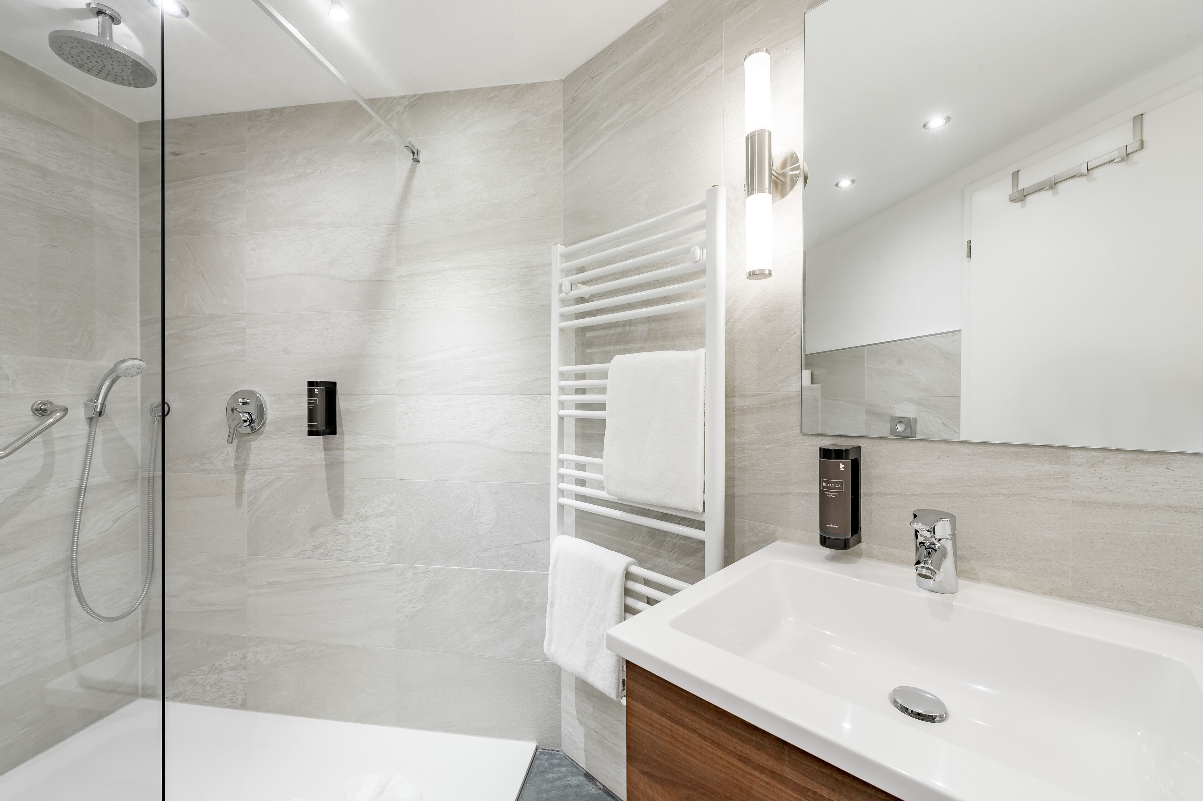 A modern bathroom with a glass-enclosed shower, a white vanity with a sink, and a large mirror.
