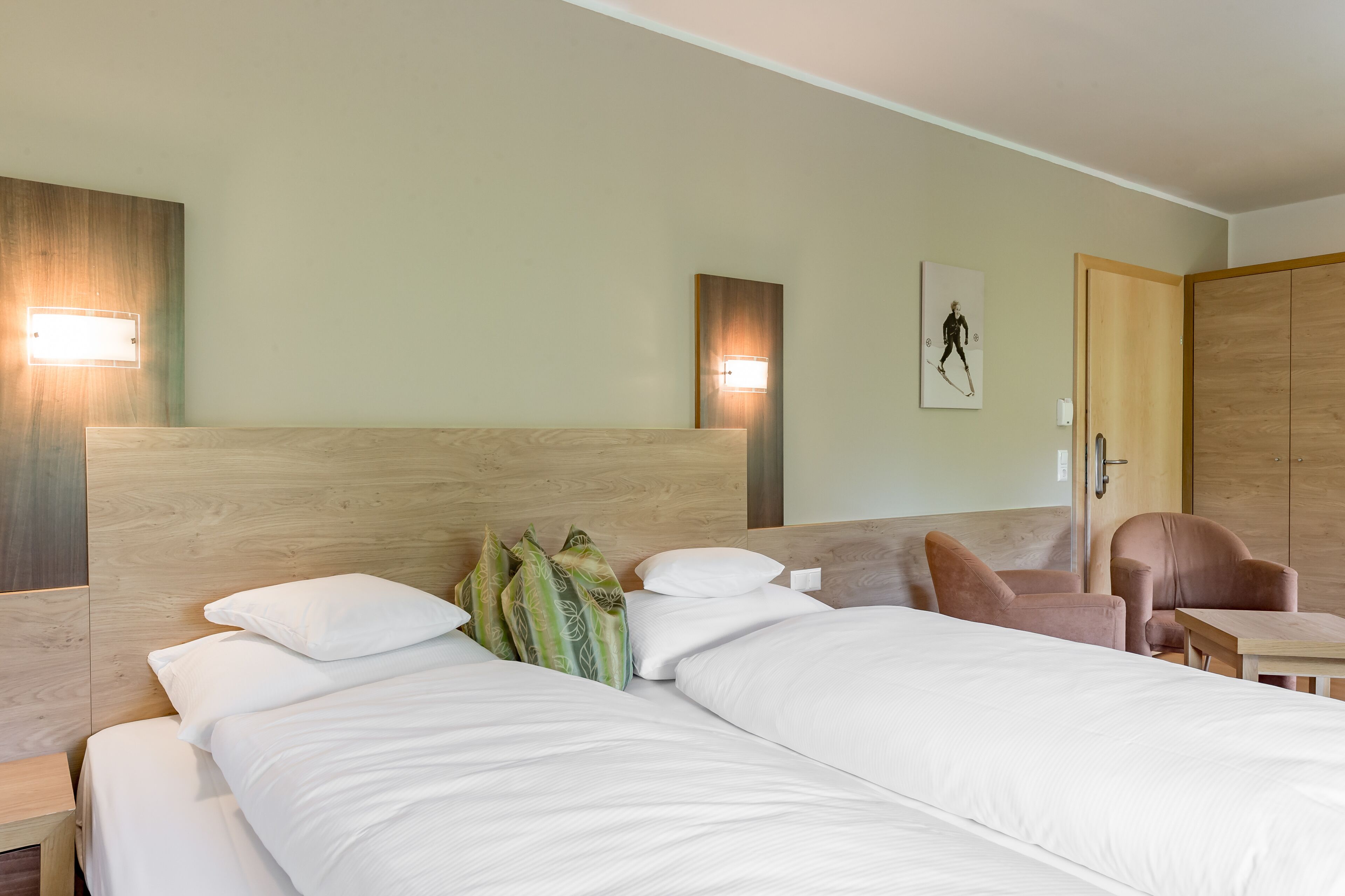 A hotel room with a large bed, two bedside tables, a wooden headboard, a wall-mounted light, a framed picture, and a wooden wardrobe.