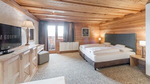 A wooden-paneled room with a bed, a TV, and a window with curtains. - Hotel zum Gourmet (Seefeld in Tirol)
