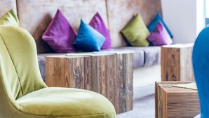 A modern living room with a green armchair, wooden side tables, and colorful cushions on a wooden bench. - Hotel zum Gourmet (Seefeld in Tirol)