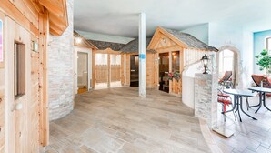 A spacious indoor area with wooden walls and stone accents, featuring a central column, a dining area with red chairs, and a stone fireplace. - Hotel zum Gourmet (Seefeld in Tirol)