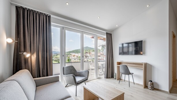 A modern living room with a sofa, two chairs, a coffee table, and a TV mounted on the wall. - Hotel zum Gourmet (Seefeld in Tirol)