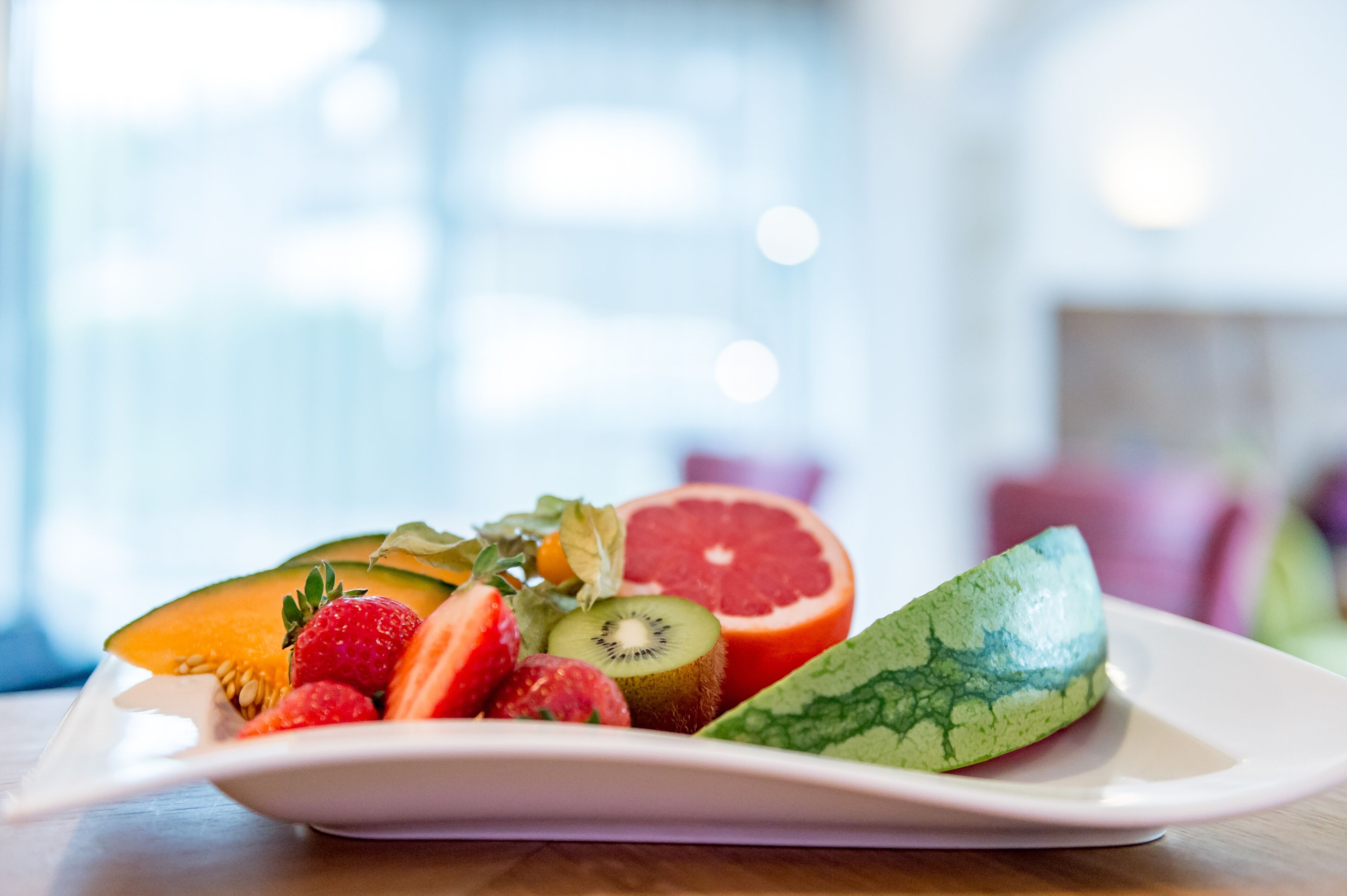 Un plato blanco con frutas cortadas, entre ellas sandía, kiwi, fresas y pomelo.