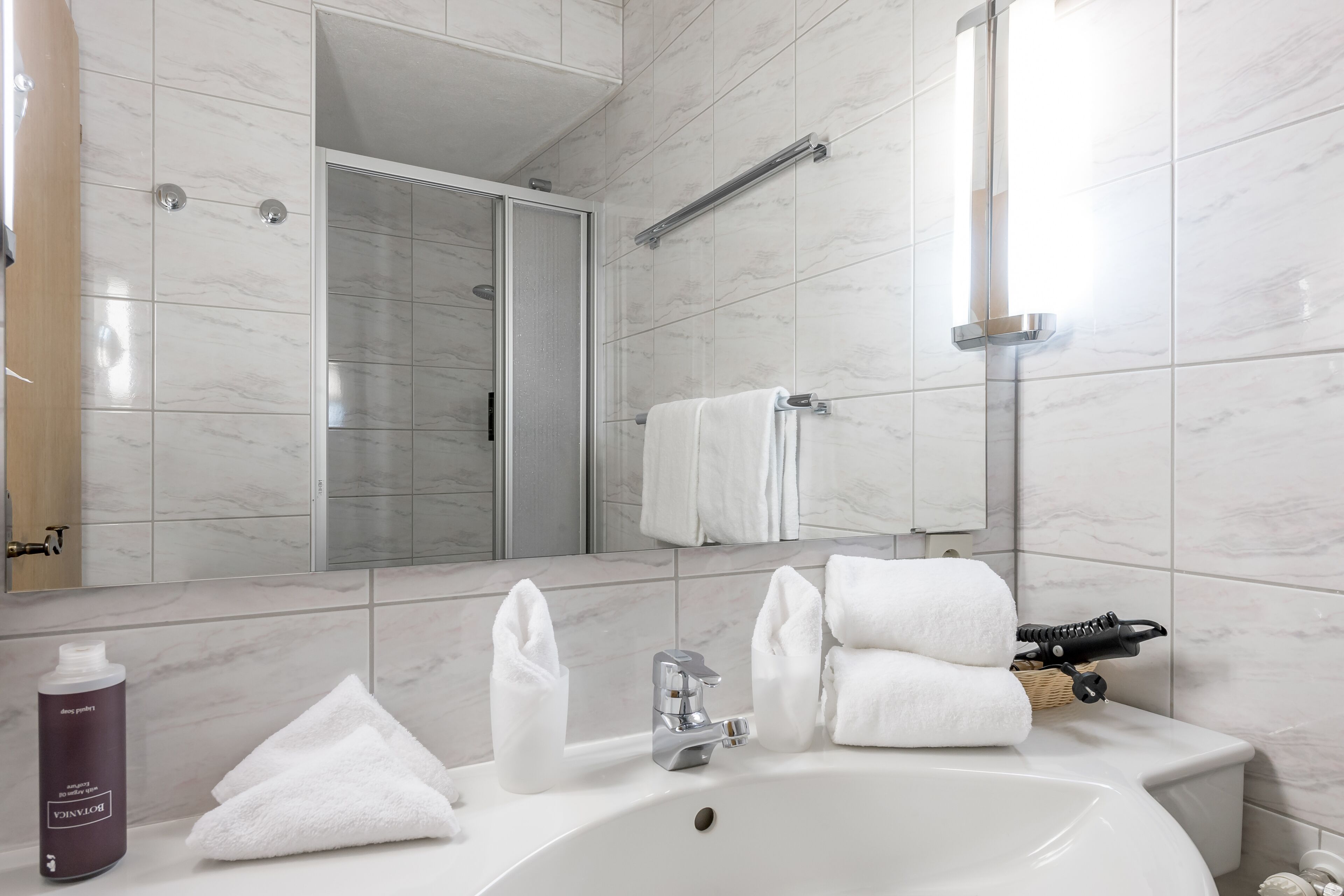 Un baño moderno con un lavabo blanco, un espejo, ducha y toallero.