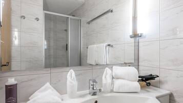 Un baño moderno con un lavabo blanco, un espejo, ducha y toallero.