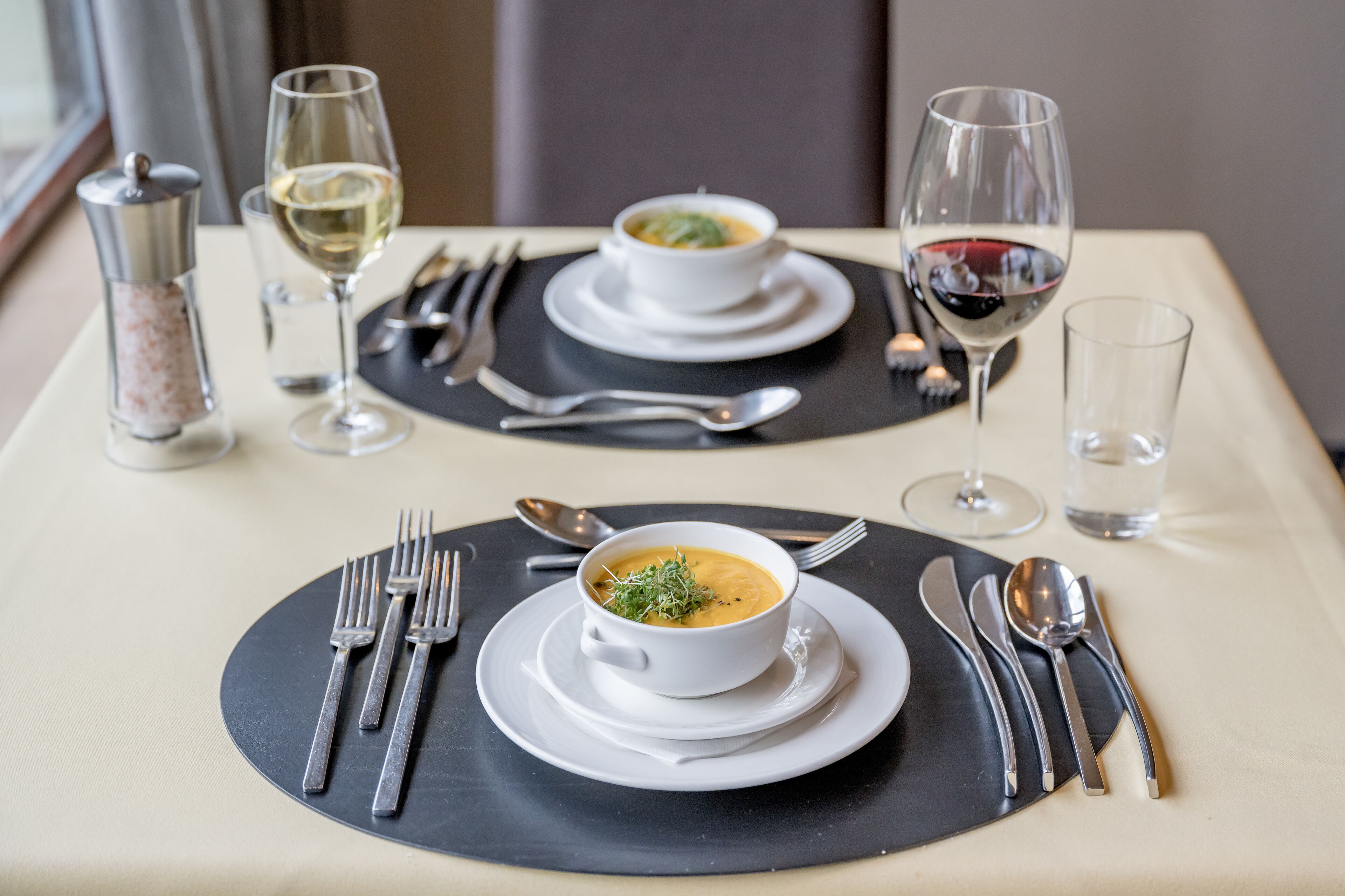 A table set with a bowl of soup, two wine glasses, and cutlery.