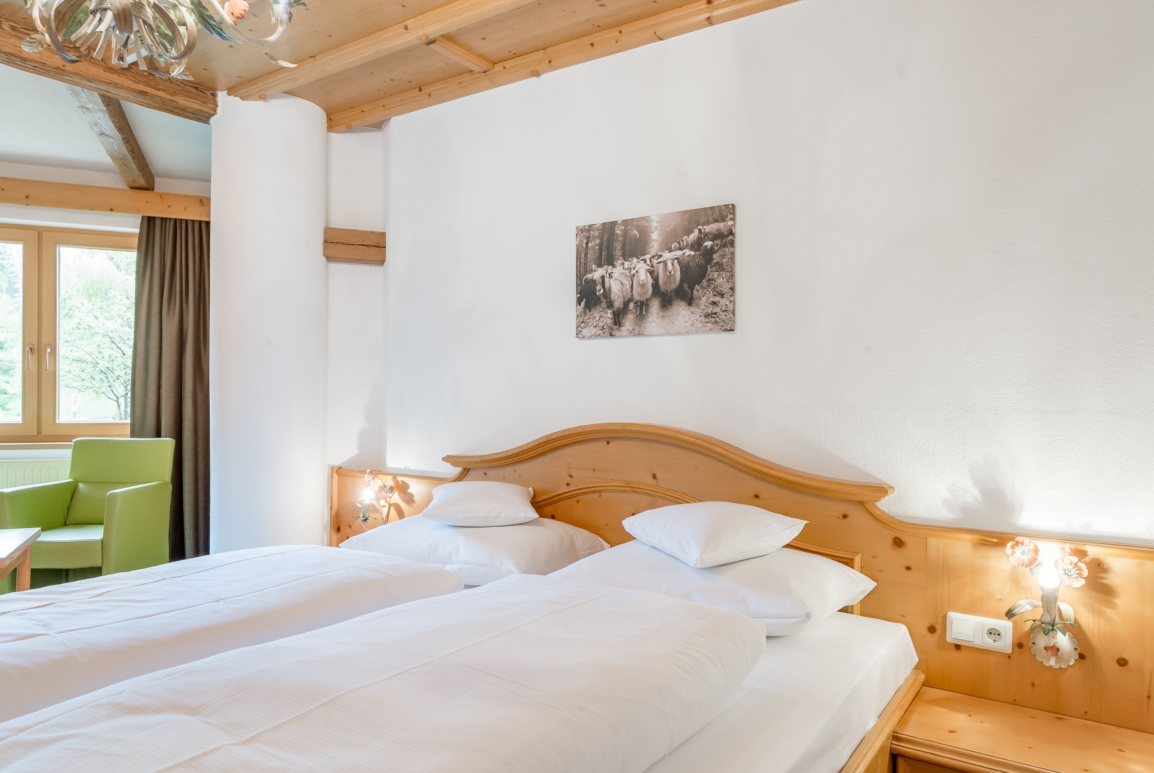 A hotel room with two beds, a wooden headboard, a green chair, and a window with curtains.