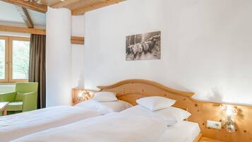 A hotel room with two beds, a wooden headboard, a green chair, and a window with curtains.