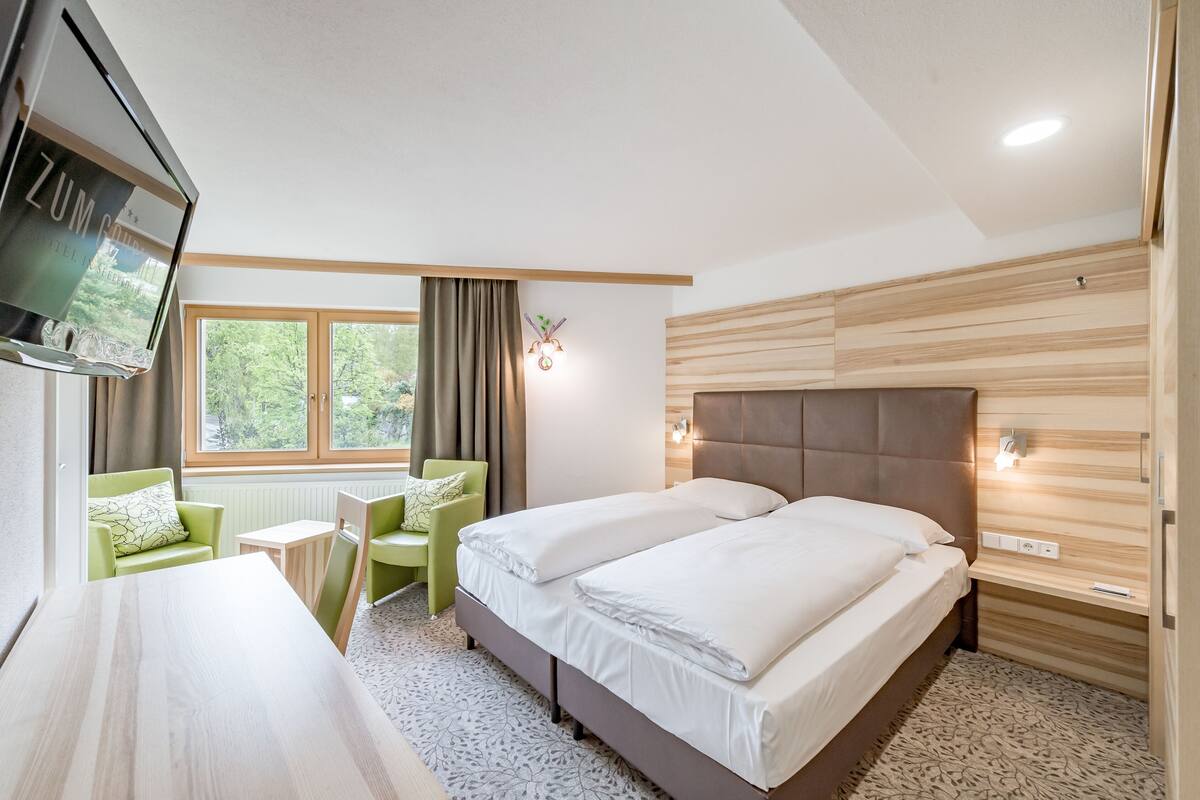 A modern hotel room with a bed, a desk, a chair, a TV, and a window with curtains.