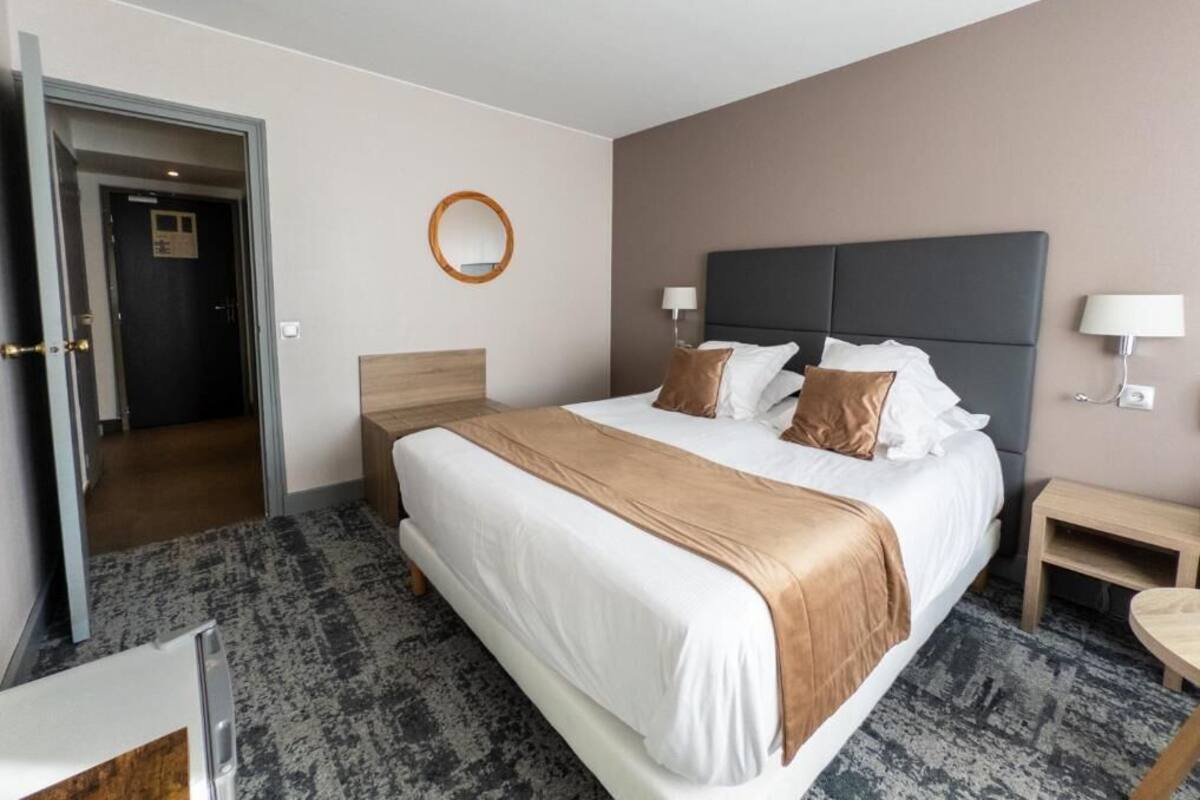A hotel room with a large bed, a bedside table, a lamp, and a door leading to another room.
