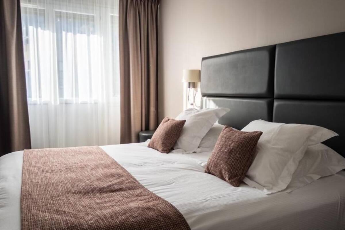A neatly made bed with a dark headboard, white bedding, and brown throw pillows.