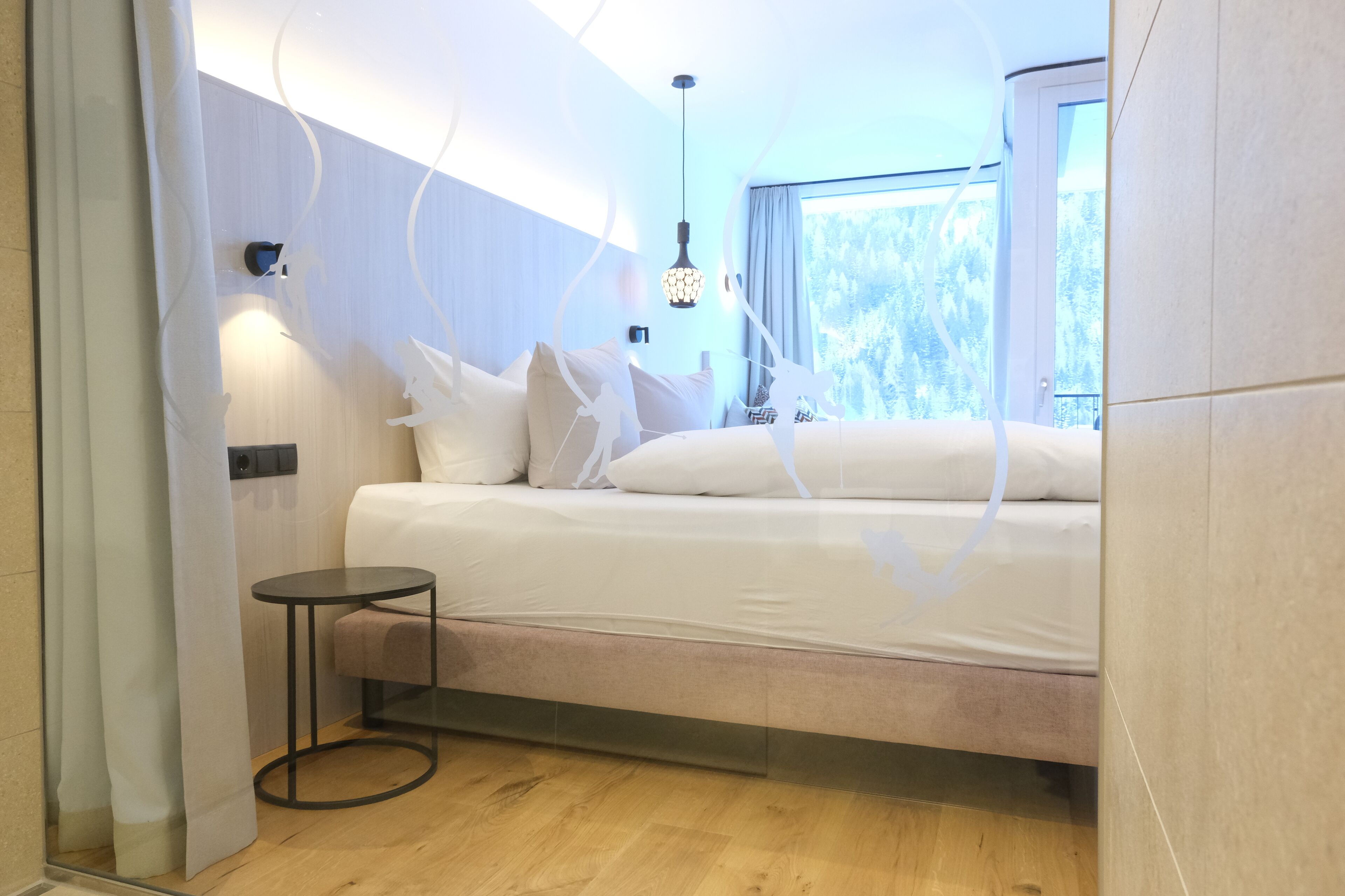 A modern bedroom with a bed, bedside table, and a window with a view of trees.