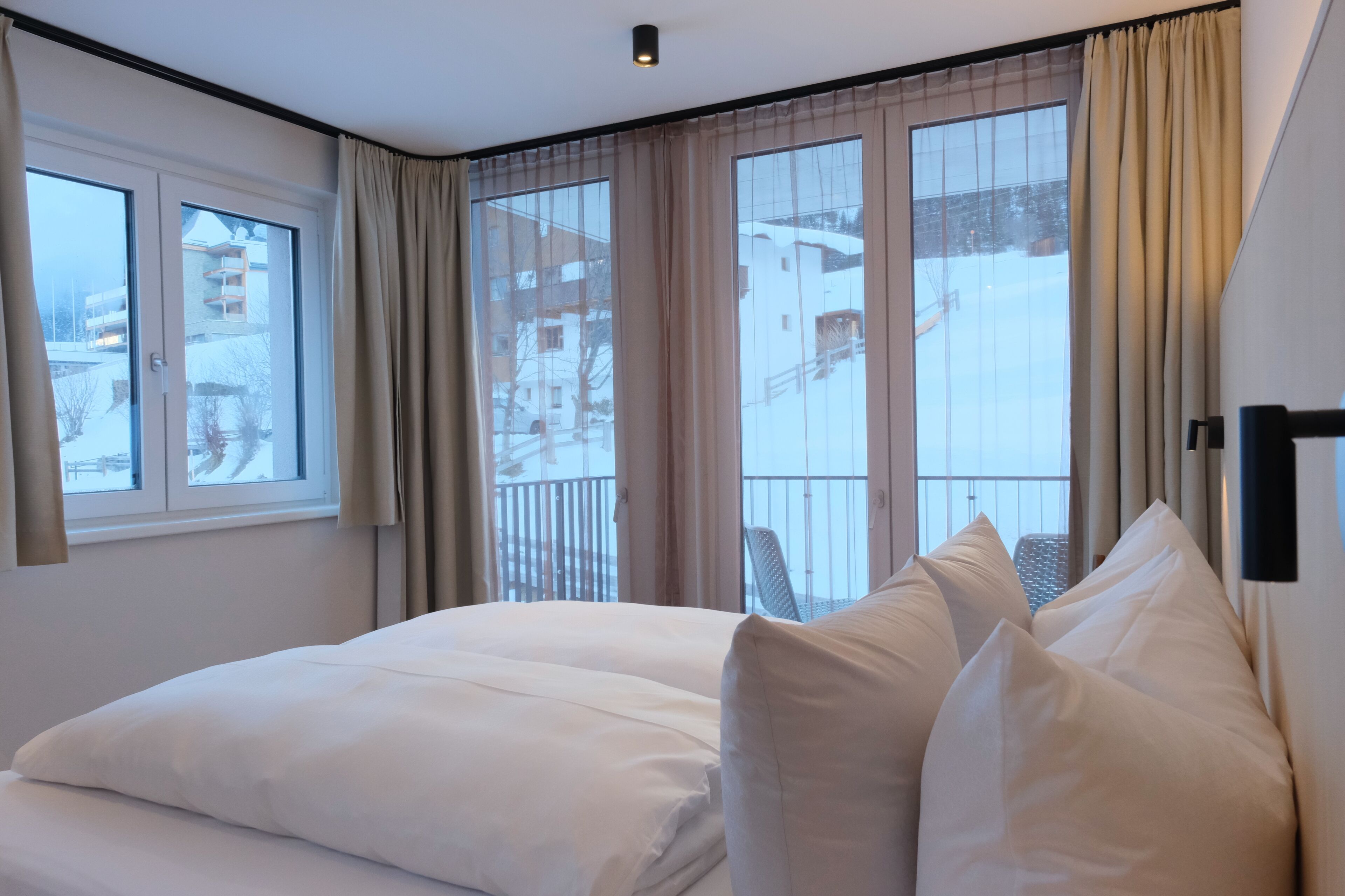 Une chambre d’hôtel avec un grand lit, une fenêtre avec des rideaux et une vue sur un paysage enneigé.