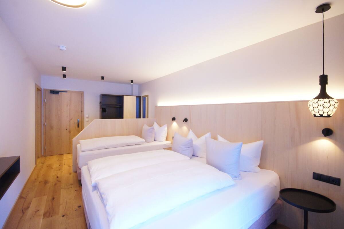 A hotel room with two beds, a small table, and a wooden floor.
