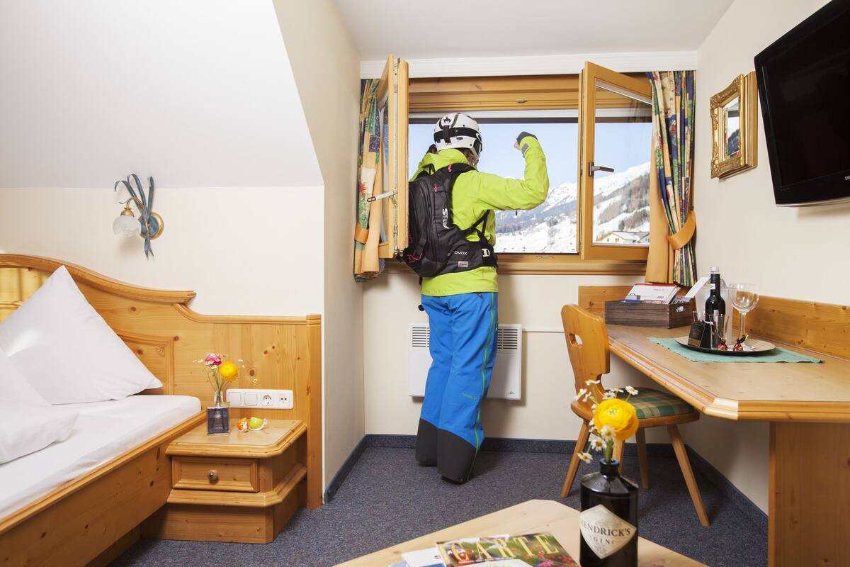 A hotel room with a bed, a desk, a chair, a window with a view of snow-covered mountains, and a television on the wall.