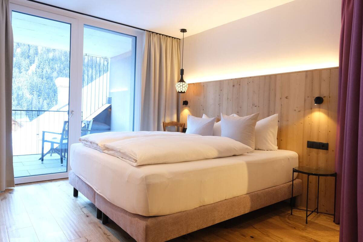 A bedroom with a bed, a sliding glass door to a balcony, and a small table.
