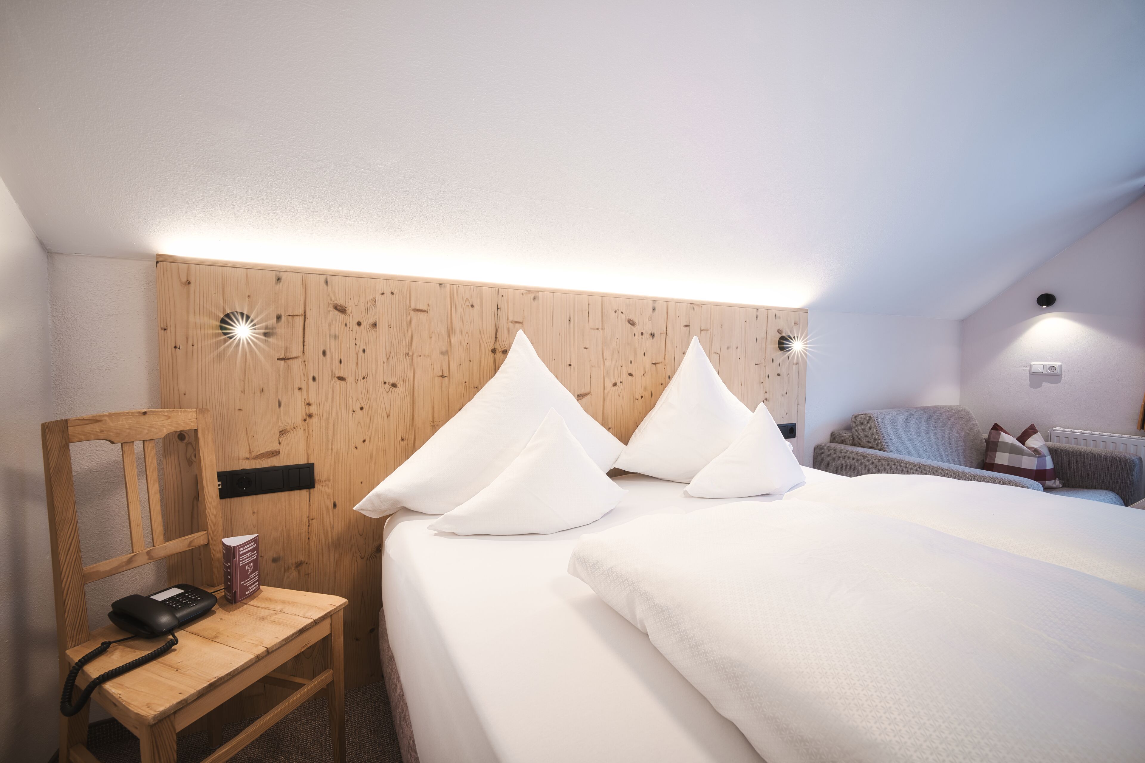 Un dormitorio con cabecera de madera, mesita de noche con teléfono y cama con ropa blanca.
