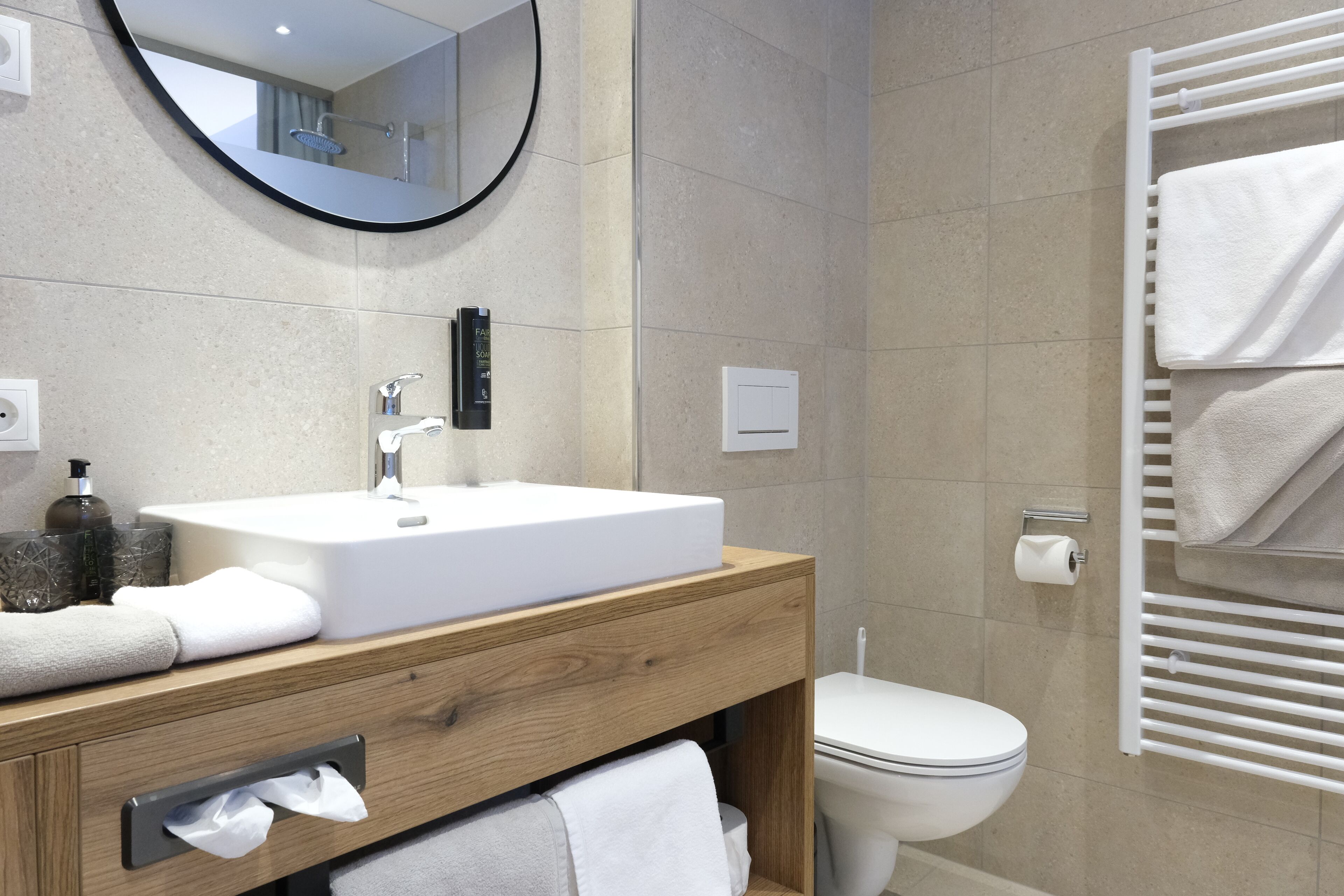 Un baño moderno con tocador de madera, lavamanos blanco y perchero para toallas.