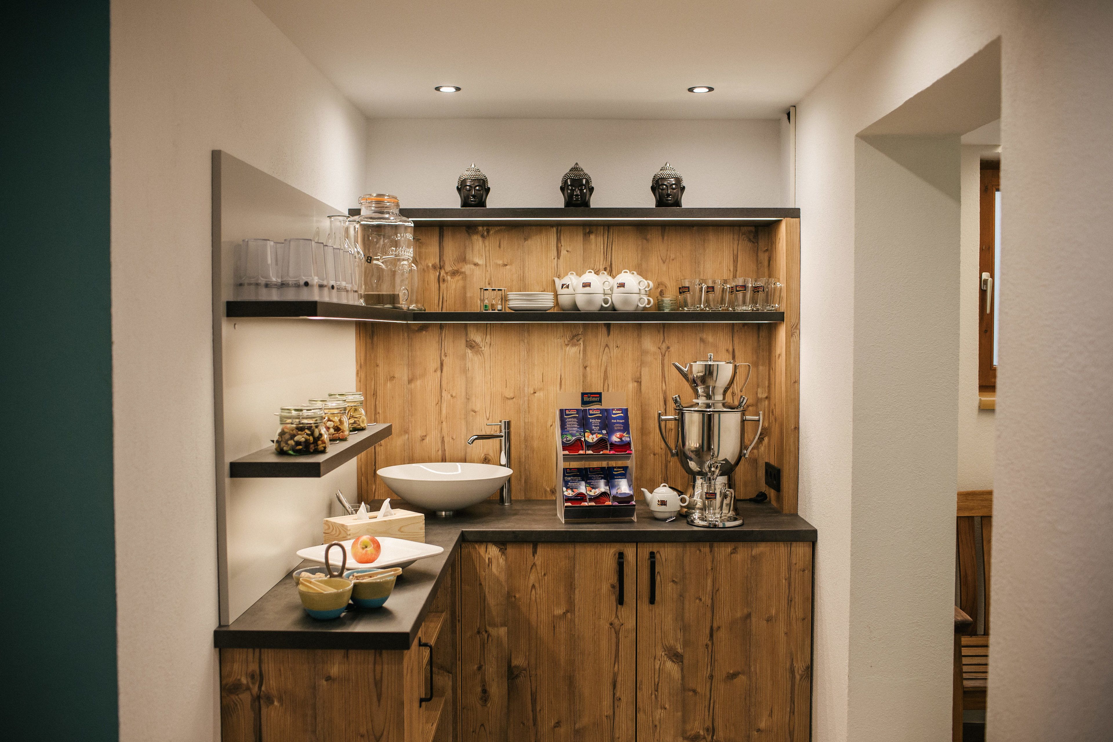 A modern kitchen with wooden cabinetry, a white sink, and shelves with kitchenware and decorative items.