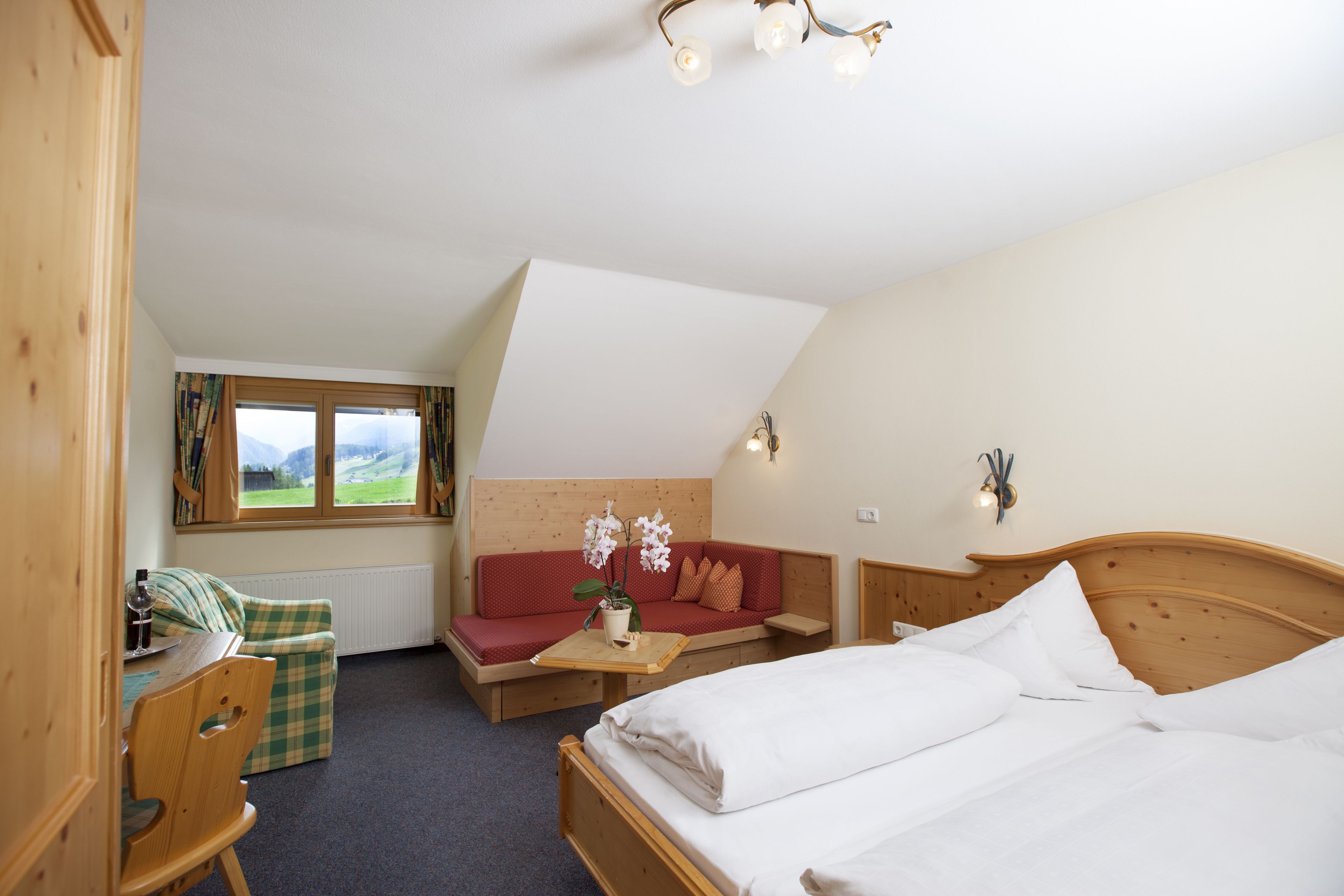 Ein gemütliches Zimmer mit einem Bett, einem Holztisch, einem roten Sofa und einem Fenster mit Vorhängen.