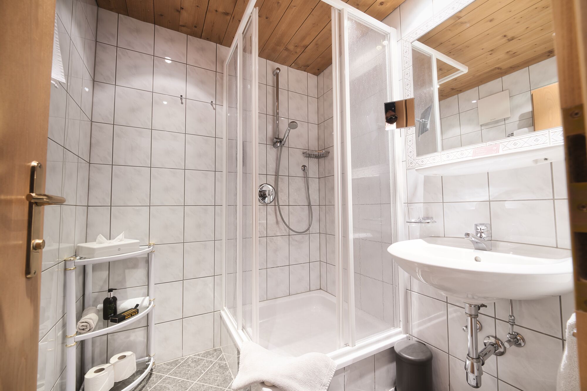 A modern bathroom with a glass-enclosed shower, a white sink, and a marble-tiled floor.