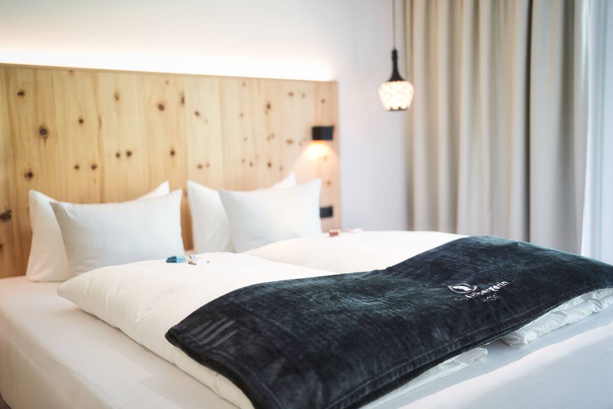 A hotel room with a wooden headboard, white bedding, and a black throw blanket.