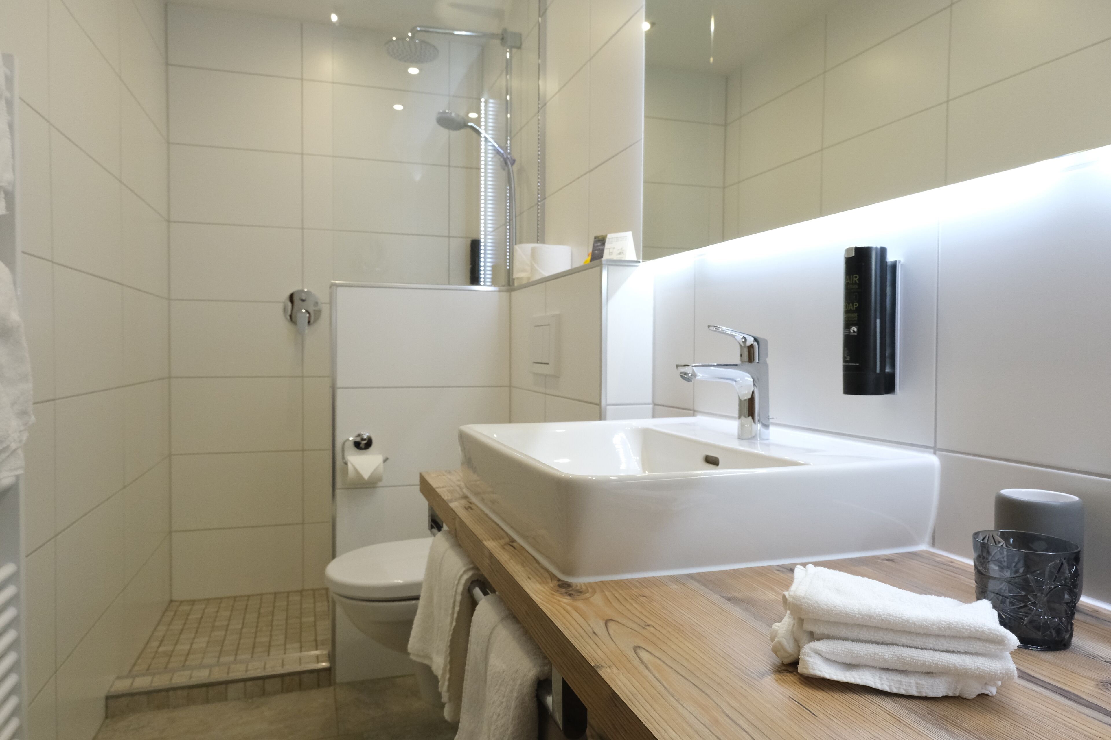 A modern bathroom with a white sink, wooden vanity, and a glass shower enclosure.