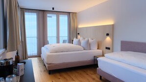 Ett modernt hotellrum med en stor säng, en mindre säng, ett skrivbord med en kaffebryggare och utsikt över omgivningarna genom stora fönster.