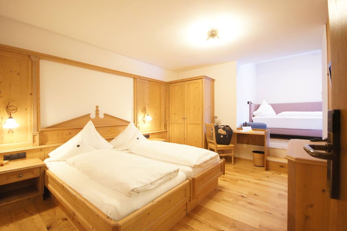 A wooden four-poster bed with white linens, a wooden nightstand with a lamp, and a wooden wardrobe.
